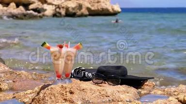 埃及海滩上的一种带稻草的玻璃中的热带鲜榨果汁矗立在海边的岩石上。 慢动作